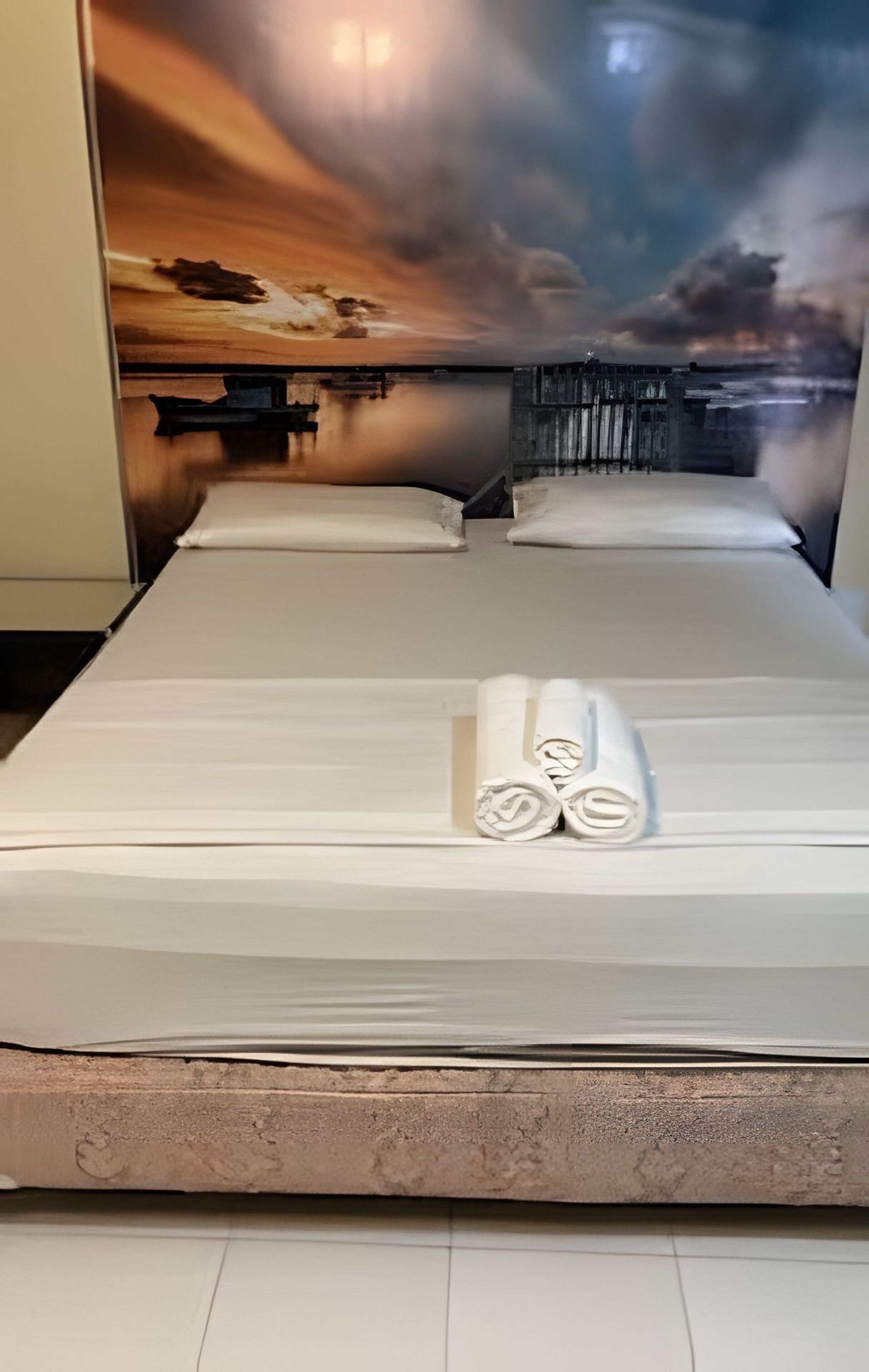 Quarto de hotel com cama, almofadas e um mural na parede.
