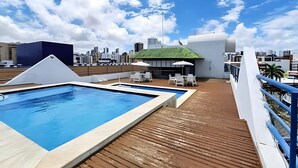 En pool på taket med utsikt över staden, ett avskärmat sittområde och ett trädäck.