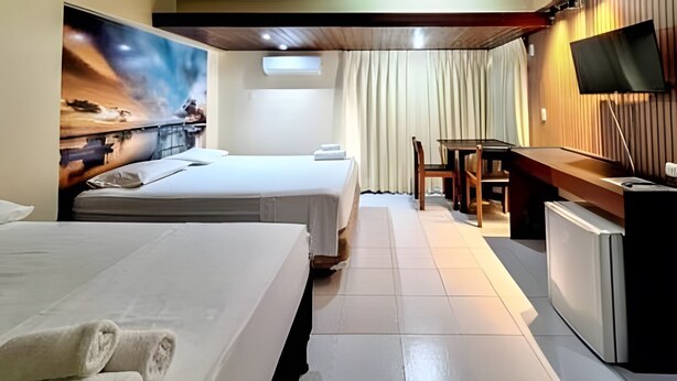 Ett hotellrum med två sängar, ett skrivbord, en tv och en tavla på väggen.
