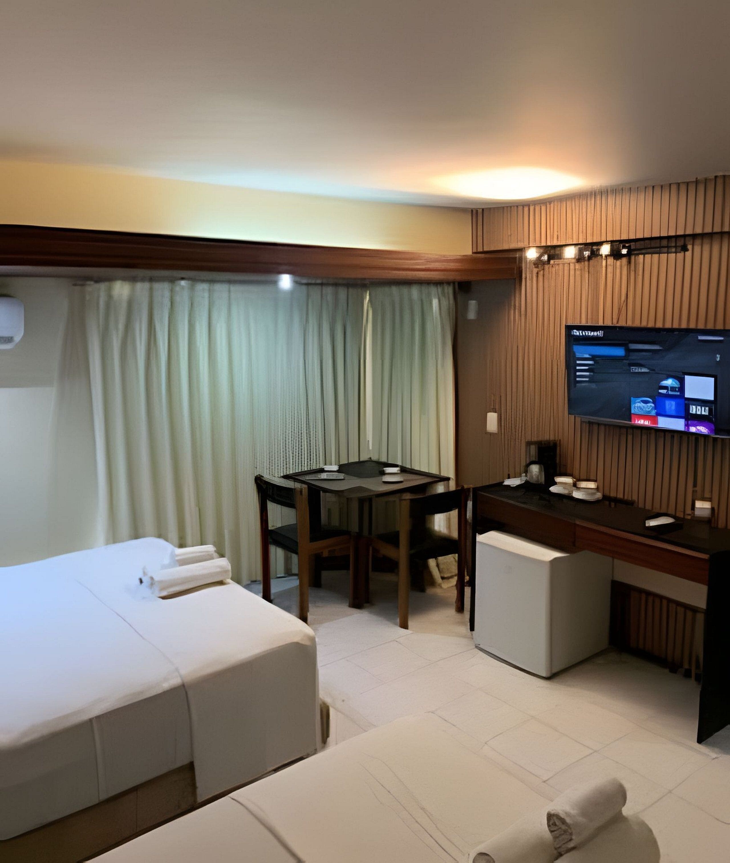 Ein Hotelzimmer mit einem Bett, einem Schreibtisch, einem Stuhl, einem Fernseher und einem Vorhang.