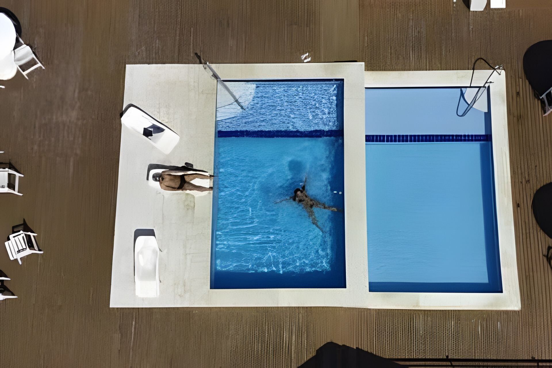 An aerial view of a swimming pool with two separate sections, a lifeguard chair, and lounge chairs.