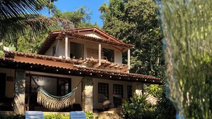Una casa de dos pisos con piscina, una hamaca y dos sillas de descanso.