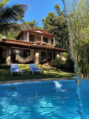Ein zweistöckiges Haus mit Swimmingpool, einer Hängematte und zwei Liegestühlen.