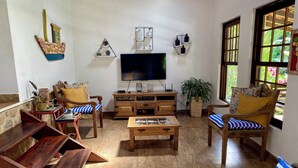 Un salón con televisor, muebles de madera, una planta en maceta y una ventana con vistas.