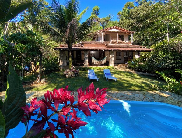 A house with a pool, surrounded by lush greenery and palm trees.