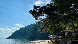 Una playa con zona de restaurante, mesas al aire libre y sombrillas.