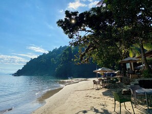 Ein Strand mit Restaurantbereich, Sitzgelegenheiten im Freien und Sonnenschirmen.