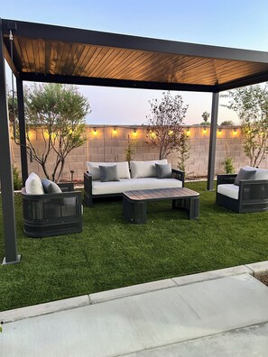 Eine Außenpatio mit einer Holzpergola, einer Couch, zwei Sesseln und einem Couchtisch.