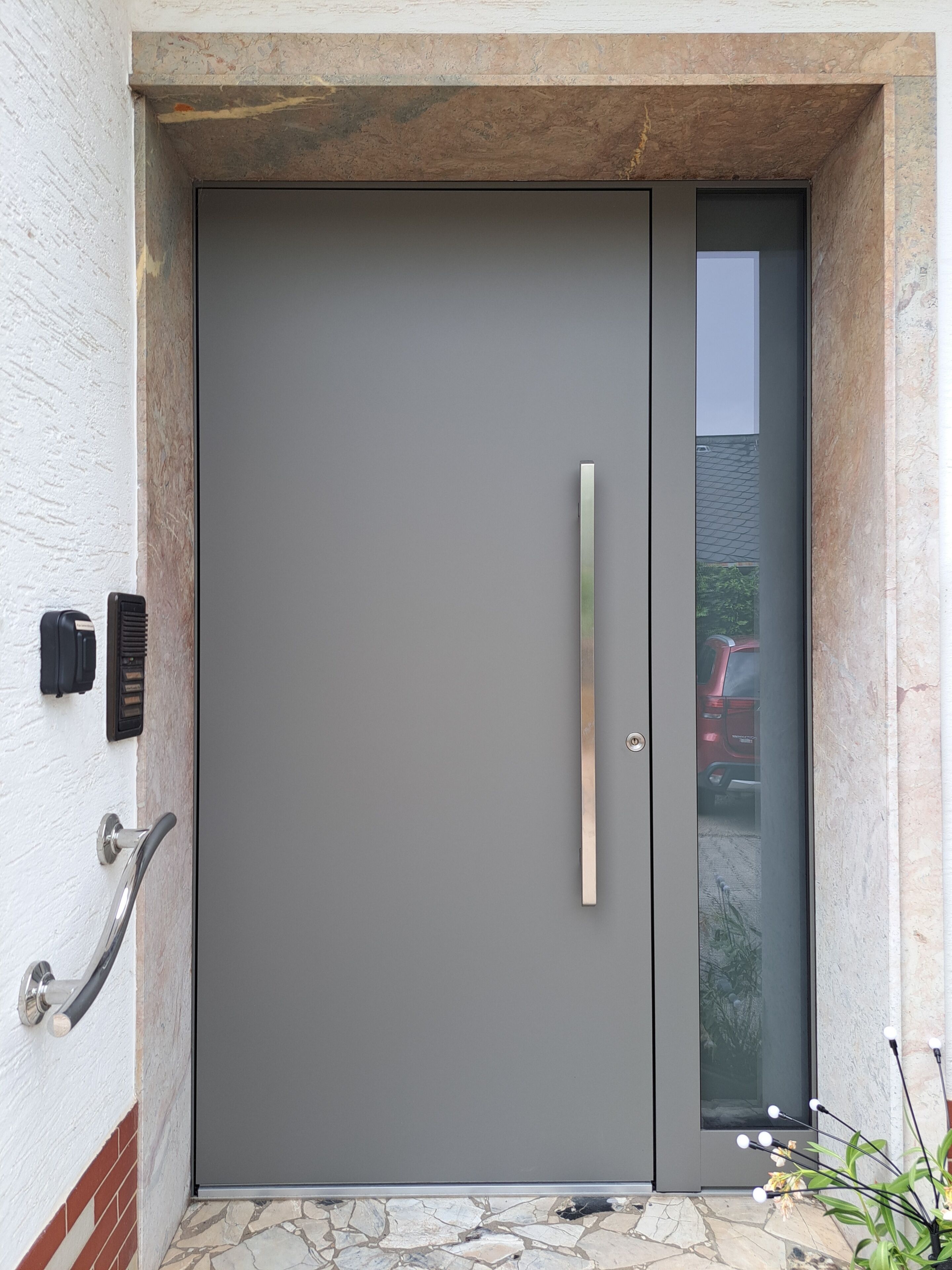 A modern door with a handle, a peephole, and a keypad on the wall.
