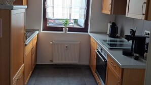 A compact kitchen with wooden cabinets, a built-in stove, a window with curtains, and a radiator. - Rieslingglück Vacation Rental (Trittenheim)
