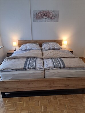 A double bed with a wooden frame, two bedside tables with lamps, and a wall-mounted painting. - Rieslingglück Vacation Rental (Trittenheim)