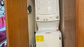 A compact laundry room with a front-loading washing machine, a dryer, and a wooden cabinet above. - Perfect 1-bedroom apartment with AC in welcoming Puerto Aventuras (Puerto Aventuras)