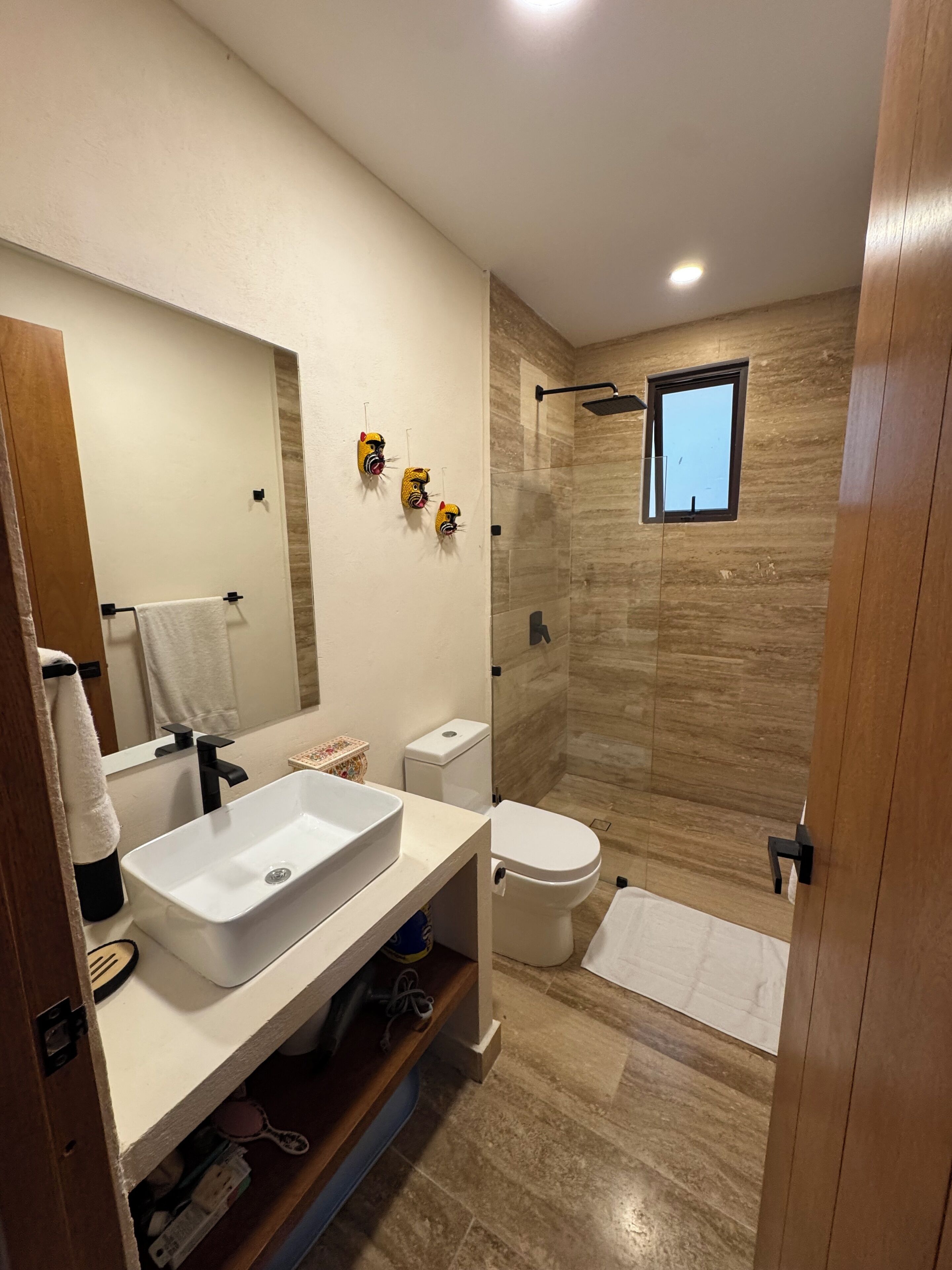 Ein modernes Badezimmer mit großem Spiegel, Waschbecken in Weiß, Toilette und Duschbereich.