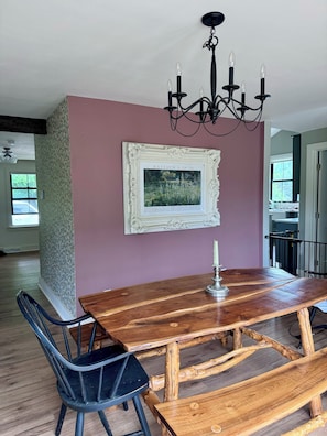 A dining area with a wooden table, chairs, a chandelier, and a framed picture on the wall. - Eden Estates — Family Travel, Elevated. (Rexford)