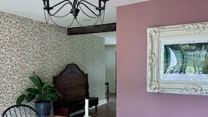 A dining area with a wooden table, bench, chandelier, potted plant, and a framed picture on the wall.