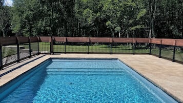 Piscina rectangular con agua azul cristalina, rodeada por una terraza de madera y una cerca de metal negro.