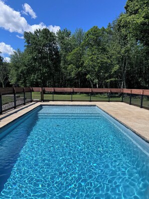 A rectangular swimming pool with clear blue water, surrounded by a wooden deck and a black metal fence. - Eden Estates — Family Travel, Elevated. (Rexford)
