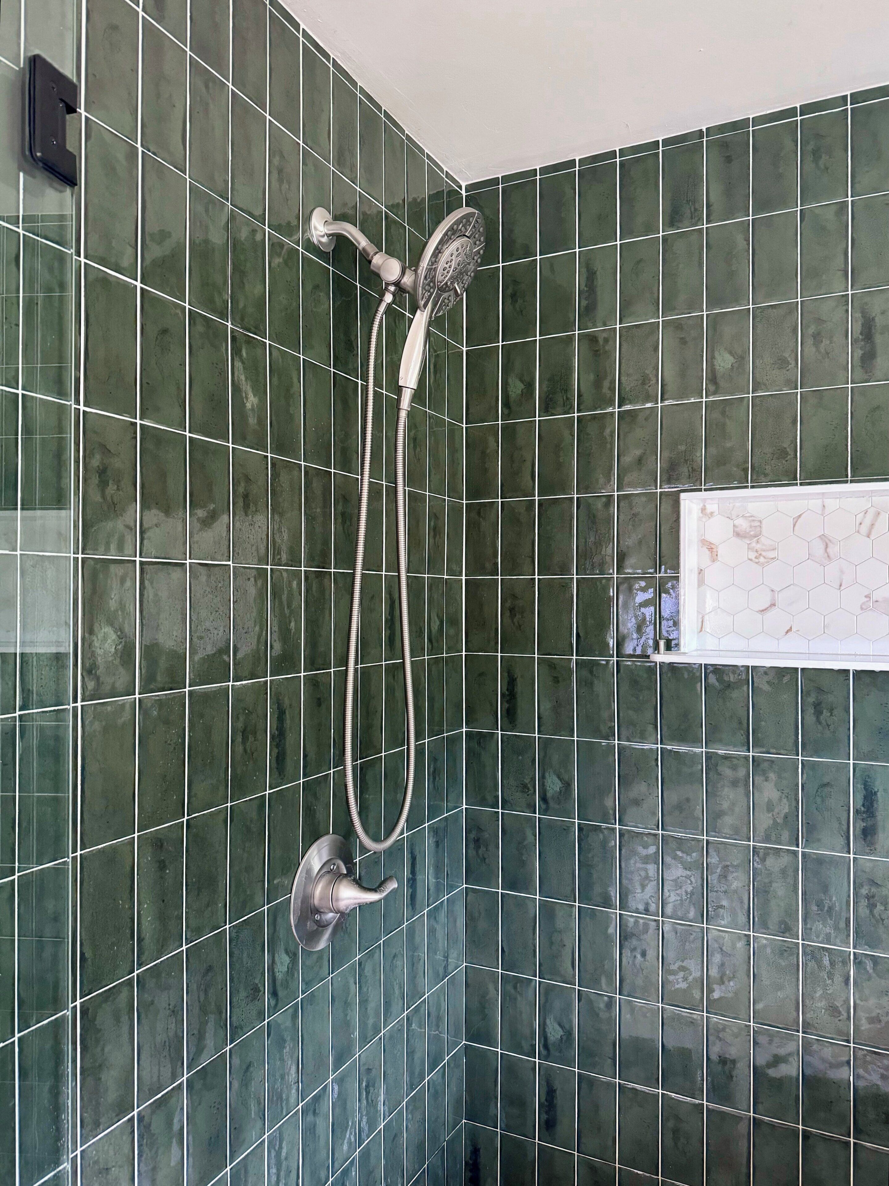 Een badkamer met groene betegelde wanden, een douche met een handdouche en een klein raam met honingraatmotief tegels.