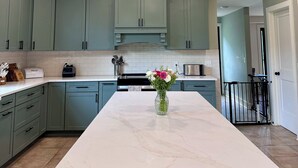 A kitchen with a central island, light green cabinets, a ceiling fan, and recessed lighting.