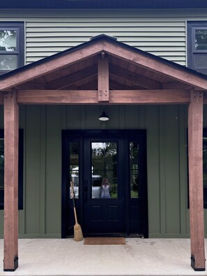 A building entrance with a wooden porch, a black door, and a broom leaning against the wall.