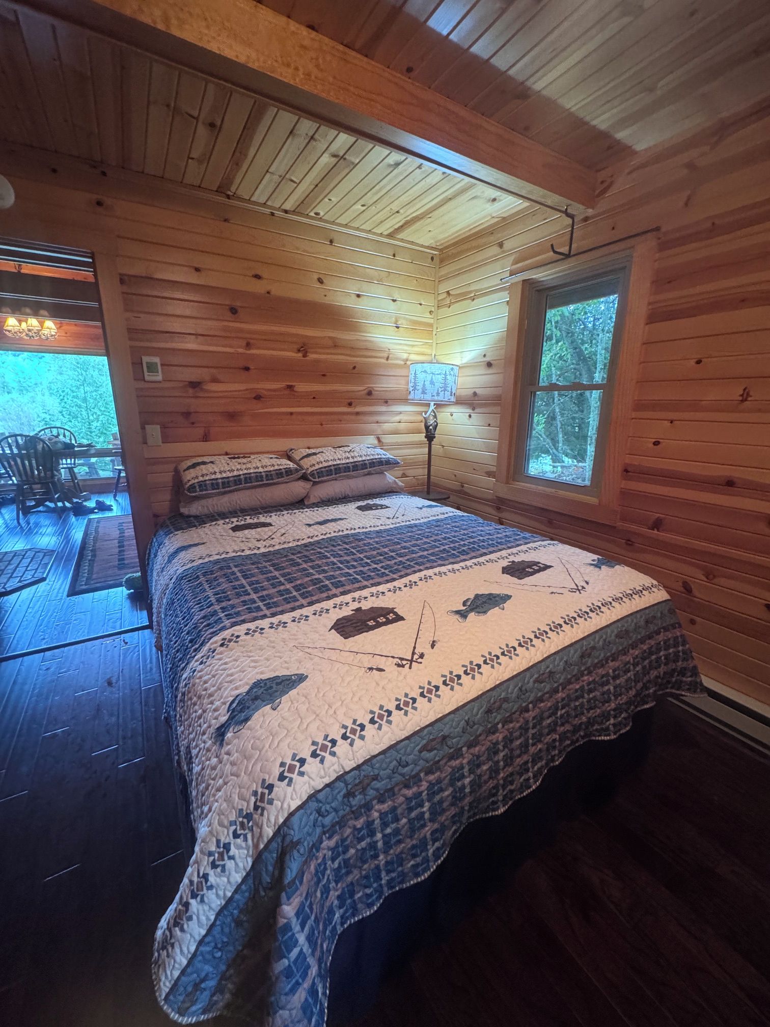 A wooden cabin bedroom with a bed, a window, and a view of the outdoors.