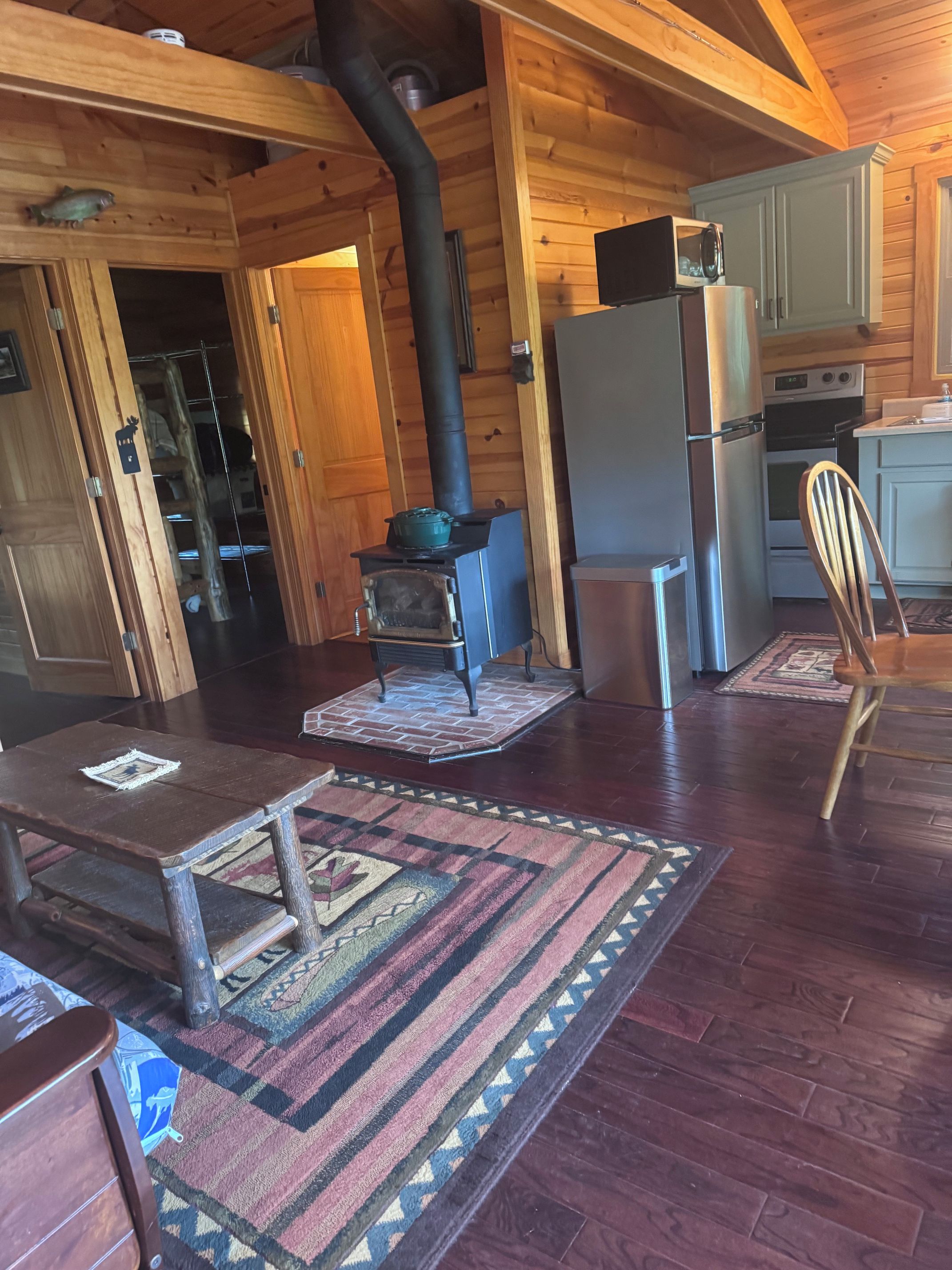 A wooden cabin interior with a wood-burning stove, a refrigerator, and a microwave.