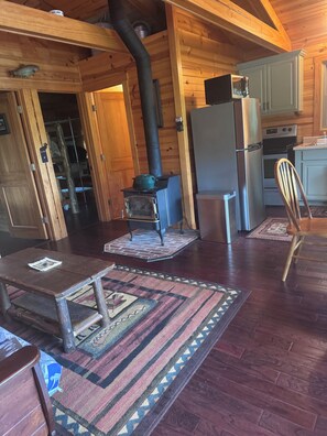 A wooden cabin interior with a wood-burning stove, a refrigerator, and a microwave. - Serene 2-bedroom cabin on Little Manistee River -Fisherman's paradise (Manistee)