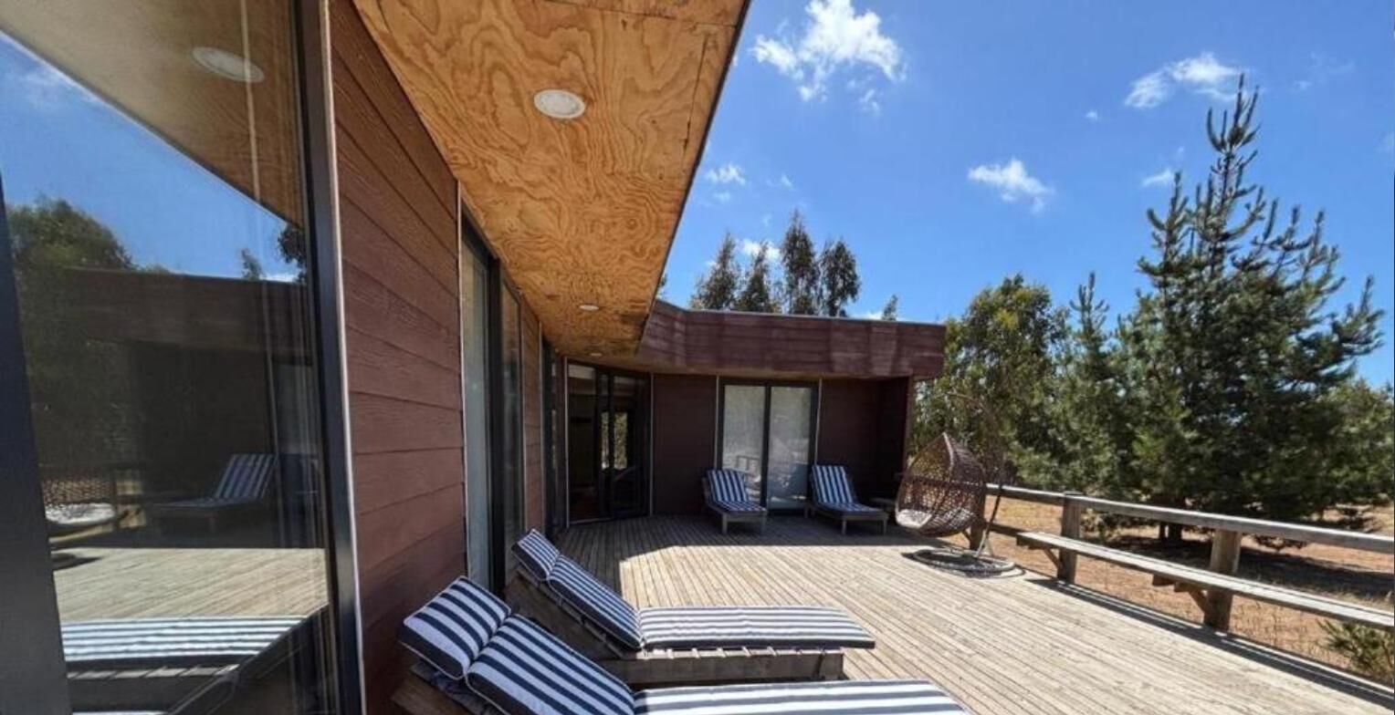 A modern building with a wooden deck, lounge chairs, and a clear view of trees.