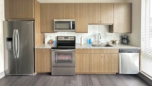 A modern kitchen with stainless steel appliances, wooden cabinets, a granite countertop, and a dishwasher. - Luxury Studio Apartment - 10 mins from Downtown (Houston)