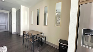 A modern kitchen with a stainless steel refrigerator, a dining table with chairs, and a trash bin. - Luxury Studio Apartment - 10 mins from Downtown (Houston)