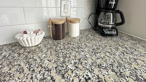 A kitchen with white subway tiles, a granite countertop, a coffee maker, and two jars. - Luxury Studio Apartment - 10 mins from Downtown (Houston)