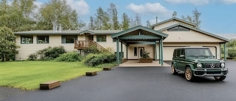 A two-story house with a covered porch, a driveway, and a green car parked in front.
