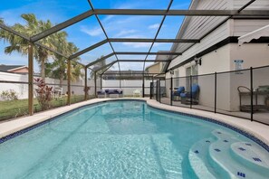 A swimming pool with a covered area, lounge chairs, and a view of a residential building.