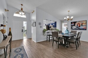 A modern kitchen with blue cabinets, a dining area with a wooden table and chairs, and a hallway with a white door.