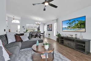 A modern living room with a sofa, coffee table, TV, and dining area.