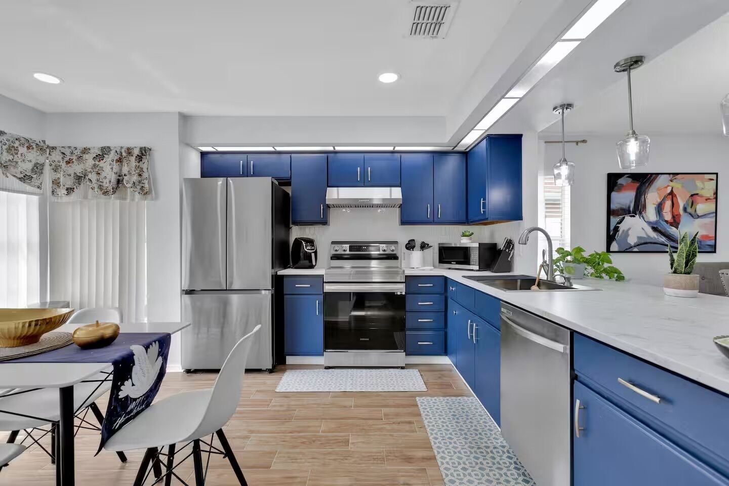 Una cocina moderna con armarios azules, electrodomésticos de acero inoxidable y un comedor con mesa y sillas.