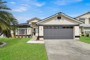 A residential house with a garage, a well-maintained lawn, and a palm tree. - Florida Vacation Home by Parks! (Kissimmee)