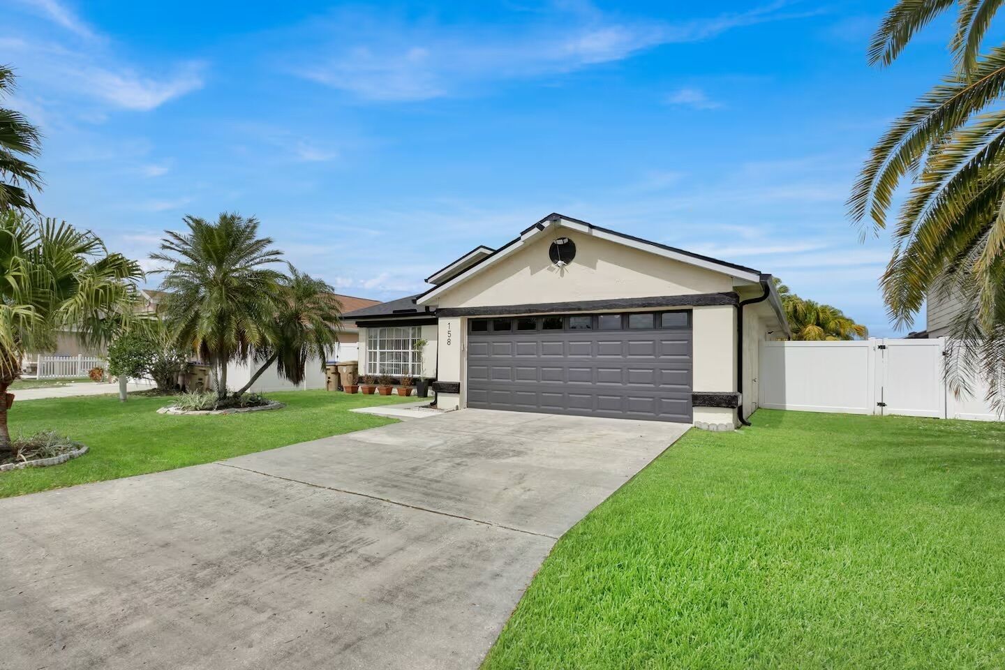 A single-story house with a garage, a well-maintained lawn, and palm trees.
