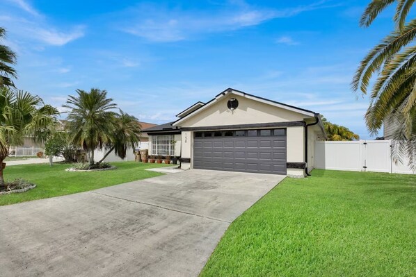A single-story house with a garage, a well-maintained lawn, and palm trees.