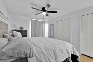 A bedroom with a bed, a ceiling fan, a dresser, and a window with curtains.