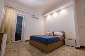 Ein Schlafzimmer mit Bett, Nachttisch, Fenster mit Jalousien und Klimaanlage.