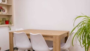 A dining area with a wooden table and four white chairs, a shelf with decorative items, and a potted plant. - Experience Palermo in total comfort: a bright, cozy, and centrally located home. (Palermo)