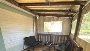 En overdækket veranda med trægulv, en bænk og et bord.