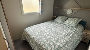 Et soveværelse med seng, et vindue med gardiner, et natbord og en lampe monteret på væggen.