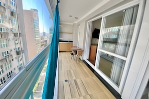 Ein Balkon mit Blick auf eine Stadtansicht, Holzboden, ein Tisch mit Stühlen und eine Schiebeglastür.