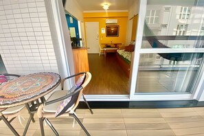 Una habitación con piso de madera, una cama, una pequeña mesa con sillas y un ventanal grande.