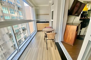 Un balcon avec un plancher en bois, une petite table avec une chaise, un meuble et un téléviseur fixé au mur.