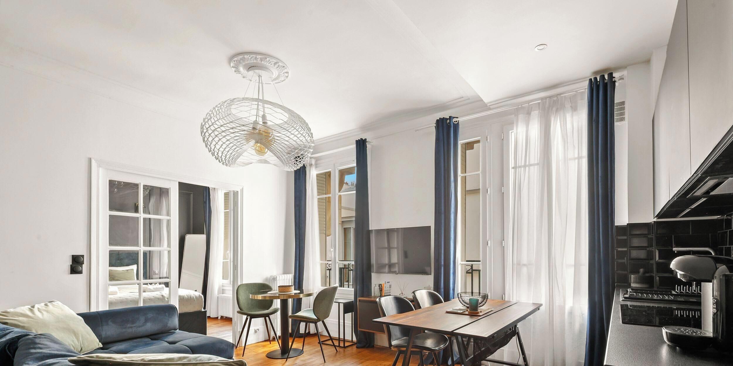 A modern living room with a sofa, dining table, chairs, and a coffee machine.