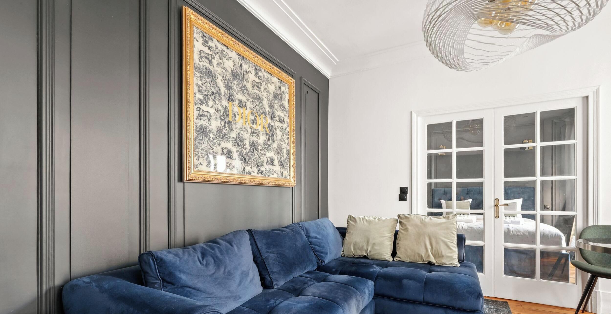 A room with a dark blue sofa, a large framed artwork on the wall, and a door with multiple windows.