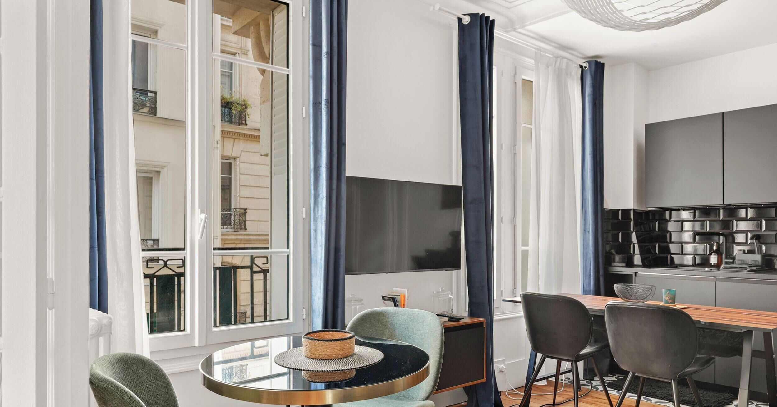 A modern kitchen with a black backsplash, a dining area with a round table and chairs, and large windows with blue curtains.